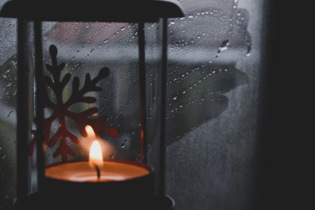 A single candle glowing against a dark winter window, symbolizing remembrance during the holiday season